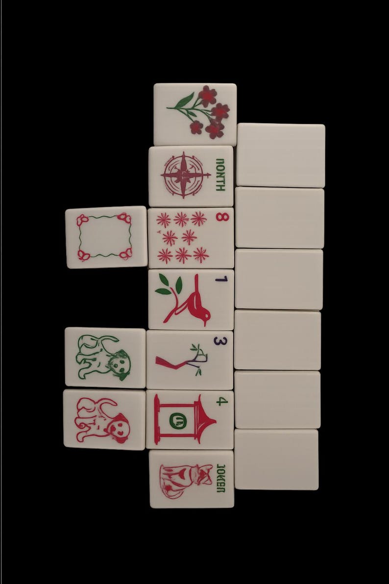 May include: A collection of white Mahjong tiles with various red and green symbols and numbers. The tiles feature images of flowers, a compass, stars, birds, and dogs. The word "NORTH" is visible on one tile, and "JOKER" on another.