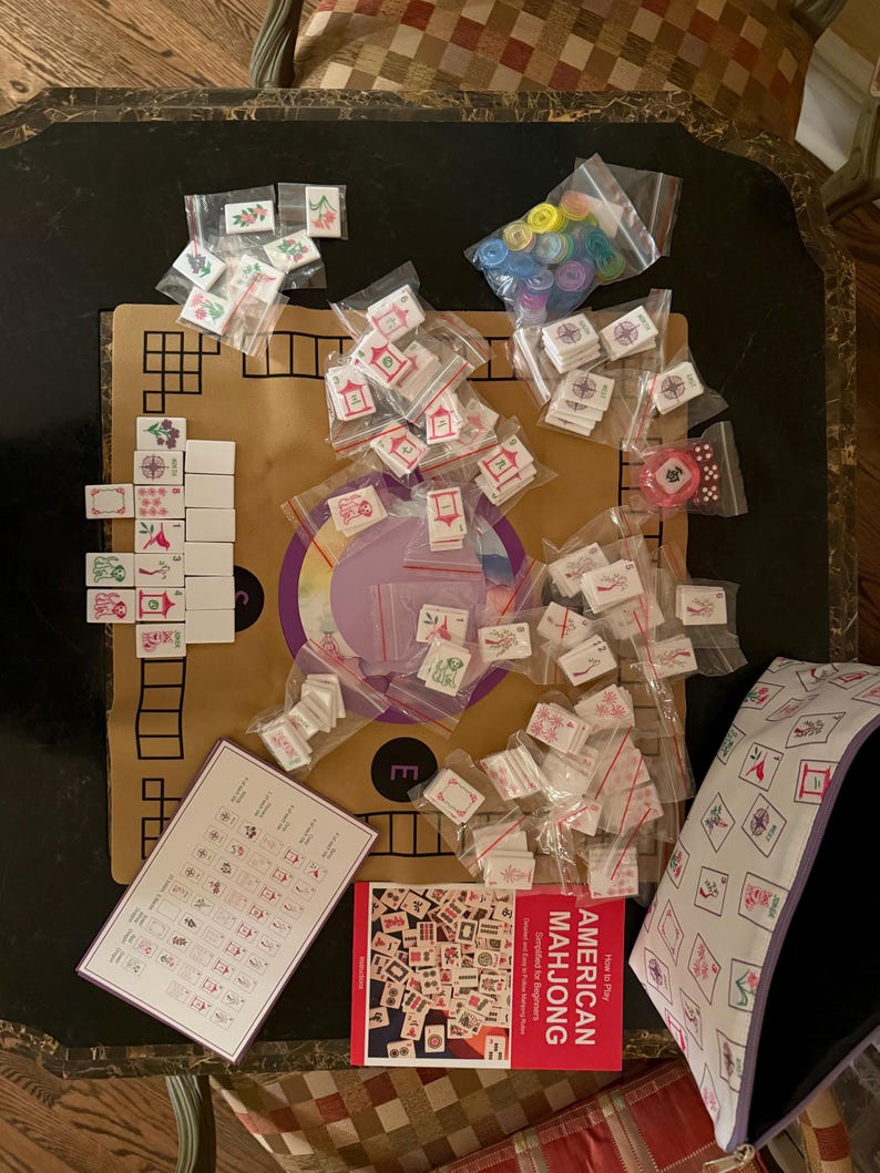 May include: An American Mahjong set with tiles, dice, and a book titled "American Mahjong". The tiles are white with red and green symbols. The set includes a purple and white carrying case and a game board.