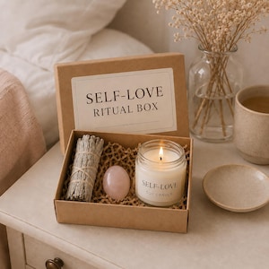 Pode incluir: Uma caixa de papelão marrom rotulada como Self-Love Ritual Box contendo um feixe de sálvia seca, uma pedra de quartzo rosa lisa e uma pequena vela em pote de vidro com um rótulo branco escrito Self-Love Soy Candle sobre papel picado.