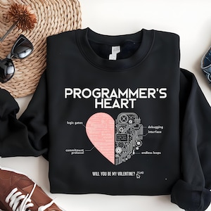 Puede incluir: Sudadera negra con el texto blanco "PROGRAMMER'S HEART". Un gráfico de corazón rosa está dividido, con un lado etiquetado "logic gates" y "commitment protocol", y el otro lado con un diseño de placa de circuito. El texto "WILL YOU BE MY VALENTINE? (Y/N)" está debajo.