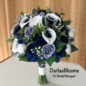 May include: A 12 inch bridal bouquet with white calla lilies, blue and white roses, and blue hydrangeas. The bouquet is wrapped in white ribbon and lace.