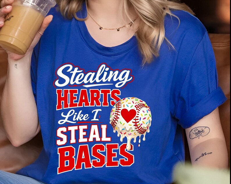 May include: Royal blue t-shirt with the text "Stealing HEARTS Like I STEAL BASES" in white and red. A baseball with a heart and sprinkles is on the right side of the shirt. The shirt is a baseball-themed design.