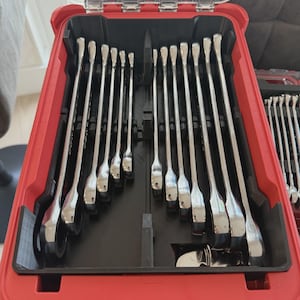 May include: A set of silver-coloured metal wrenches arranged in a red plastic carrying case with a clear, hinged lid. The wrenches are organised in vertical slots within a black interior tray, featuring various lengths and sizes of open-ended tools.