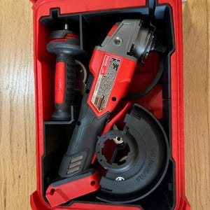 May include: A red and black power tool set, including an angle grinder and handle, stored in a red hard case. The case is open, revealing the tools neatly organized inside. The angle grinder has a silver blade guard.