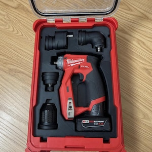 以下が含まれることがあります： 赤と黒のMilwaukee FUEL M12コードレスドリルキット、赤いケース入り。キットにはドリル、さまざまなアタッチメント、バッテリーが含まれています。ケースは開いており、ツールがきちんと整理されています。