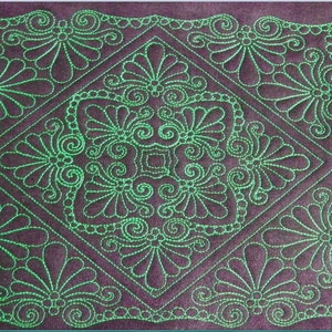 May include: A close-up of a quilt with a green embroidered design on a dark purple background. The design features a repeating pattern of swirls and leaves.