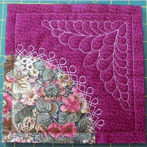 Pode incluir: Um close-up de um quadrado de tecido acolchoado com um padrão floral no canto inferior esquerdo. O resto do quadrado é de cor magenta sólida com costuras brancas em forma de folha no canto superior direito e um padrão de diamante no canto inferior direito.