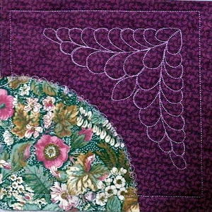 Könnte beinhalten: Gesteppter Textil mit Eckdesign. Ein weißes Federmuster ist auf einem tiefvioletten Hintergrund aufgenäht. Die linke untere Ecke zeigt einen floralen Stoff mit rosa und weißen Blumen, grünen Blättern und einem gewellten Rand.