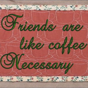May include: A rectangular, quilted placemat with a repeating pattern of coffee cups on a red background. The text "Friends are like coffee Necessary" is embroidered in green. The border features a floral pattern.