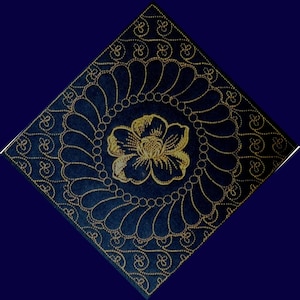 May include: A dark blue square with a gold floral design. The design features a large flower in the center surrounded by a circle of smaller flowers and a border of swirling patterns.