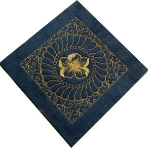 Pode incluir: Um tecido quadrado azul escuro com um desenho floral bordado em ouro. O desenho apresenta uma flor grande no centro cercada por motivos florais menores.