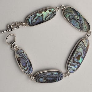 May include: A link bracelet featuring five oval-shaped abalone shell inlays set in polished silver-toned metal. The iridescent shell pieces display swirling patterns of blue, green, and purple. The bracelet secures with a silver-toned toggle clasp.