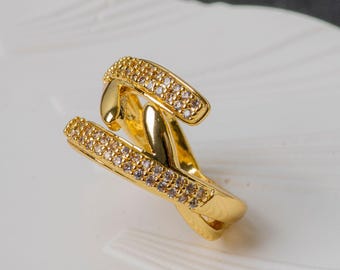 May include: A gold-toned ring featuring an open, crossover design. The two ends of the band are encrusted with small, clear, sparkling stones, while the center section remains smooth and polished gold, creating a layered, bypass-style appearance.