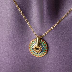 May include: Gold-toned necklace with a circular pendant. The pendant features a colorful floral design with red, green, and blue enamel. The necklace is displayed on a purple background.