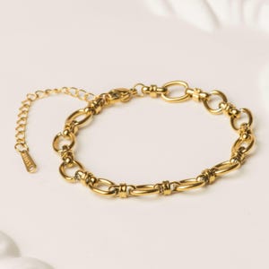 May include: A gold-colored bracelet with an adjustable chain. The bracelet features a series of oval and circular links connected by smaller, decorative bars. The clasp and chain are also gold-toned, creating a cohesive look. The bracelet is displayed on a white surface.