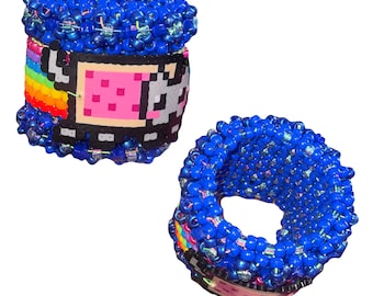 May include: Two blue beaded bracelets. One bracelet features a pixelated design with a pink square, gray and white details, and a rainbow. The other bracelet is a solid blue beaded cuff.