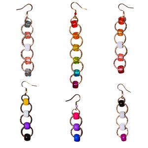 May include: Six pairs of dangle earrings with colorful beads and gold-tone metal rings. Each earring features a different color scheme, including rainbow, pink, purple, and black and white combinations. The earrings have a simple hook closure.