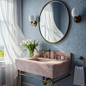 May include: A bathroom vanity with a pink marble sink and gold fixtures. A round gold-framed mirror hangs above the sink, with two sconces on either side. A vase of white tulips sits on the counter, and a white towel hangs on a gold towel ring.