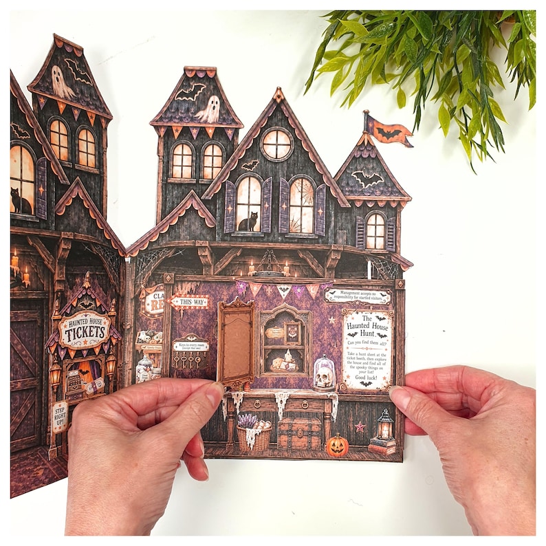 May include: A multi-paneled paper haunted house display featuring intricate illustrations of ghosts, bats, and black cats. The structure includes a ticket booth, a "Haunted House Hunt" sign, and a small hinged door that opens to reveal interior details.