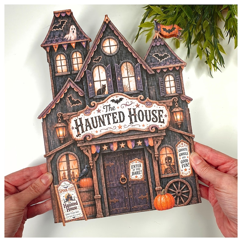 May include: A flat, die-cut paper decoration shaped like a haunted house with dark wood textures, orange pumpkins, bats, and a ghost. The sign reads The Haunted House, Enter If You Dare, and Ghosts Ghouls and Good Fun in a detailed, illustrated style.