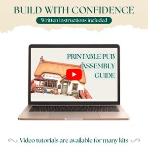 May include: A laptop screen displays a printable pub assembly guide featuring a miniature thatched-roof building labeled The Hare & Lantern. The screen includes a red play button icon, and the text reads BUILD WITH CONFIDENCE, Written instructions included, and Video tutorials are available for many kits.