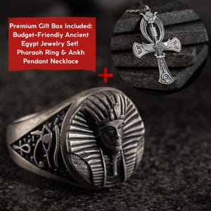 May include: A silver-toned metal ring featuring a pharaoh face relief and an ankh pendant necklace with an eye of Horus and winged design. The text reads: Premium Gift Box Included: Budget-Friendly Ancient Egypt Jewelry Set! Pharaoh Ring & Ankh Pendant Necklace.