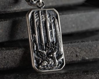 May include: A rectangular silver-toned metal pendant on a chain, featuring a detailed relief carving of a forest scene with tall trees, a deer with antlers, and a small bird resting on the ground, finished with a dark, oxidized patina.