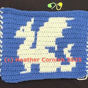 May include: A blue and white crocheted square featuring a pixelated dragon design. The dragon is white against a blue background. The edges have white fringe. Text reads "(c) Heather Cornish 2023".