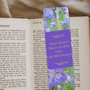 May include: A floral bookmark featuring a vibrant image of purple irises. The bookmark has a purple overlay with the quote "Where flowers bloom, so does hope." by Lady Bird Johnson.