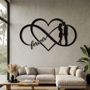 Pode incluir: Uma peça de arte de parede em metal preto que apresenta um símbolo de infinito entrelaçado com uma forma de coração. O design inclui a silhueta de duas pessoas em pé frente a frente e a palavra forever escrita em letra cursiva.