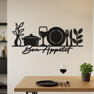 Op de afbeelding: Een zwart metalen wanddecoratie met een silhouet van een vaas met bladeren, een kookpan, een wijnglas, een bord, een vork, een mes en een tweede plant, met de tekst Bon Appétit in een cursief handschrift onder de afgebeelde items.