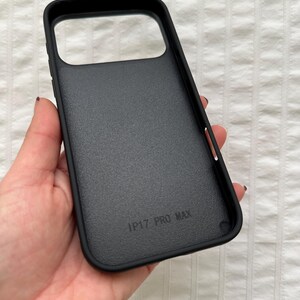 May include: Black phone case with a textured surface. The case has a rectangular camera cutout and the text "IP17 PRO MAX" printed on the inside. The case is designed to protect a phone.
