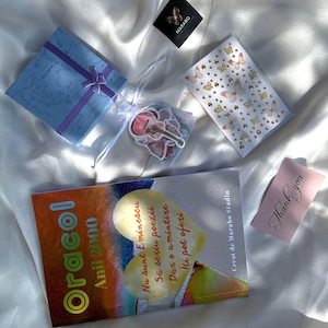 Op de afbeelding: Een lichtblauw cadeau-doosje met een paars lint, een klein wit organza zakje met stickers, een vel met vlinder- en gouden stippenstickers, een boek getiteld Oracol Anii 2000 met een hartafbeelding en een roze kaartje met de tekst Thank you.