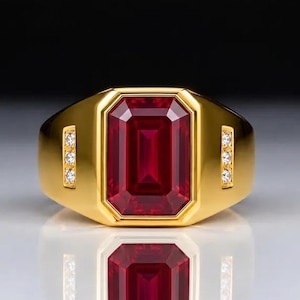 Puede incluir: Un anillo de oro con una gran piedra preciosa de color rojo intenso y corte esmeralda rectangular en el centro. La banda incluye dos acentos verticales a cada lado de la piedra principal, cada uno con tres pequeños diamantes blancos redondos.