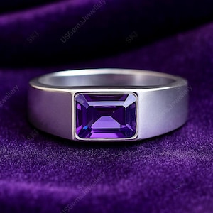 Peut inclure: Une bague en argent avec une pierre précieuse rectangulaire violet foncé. La bague a un anneau plat et un sertissage carré pour la gemme. Le fond est un tissu violet foncé riche.