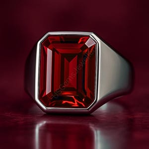 May include: A silver ring with a large, rectangular, faceted red gemstone. The gemstone is set in a bezel setting, and the band is smooth and polished. The ring is displayed against a dark red background.
