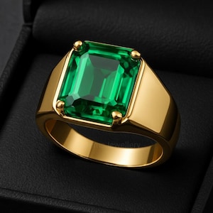 May include: A gold ring featuring a large, rectangular, emerald-cut green gemstone set in a four-prong mounting. The band is smooth and polished, showcasing a solid gold construction that highlights the vibrant green stone at the center.