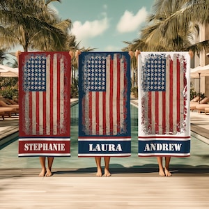 May include: Three rectangular beach towels with a distressed American flag design. Each towel features a blue field of stars and red and white stripes. The bottom of each towel has a colored band with a name: Stephanie, Laura, and Andrew.