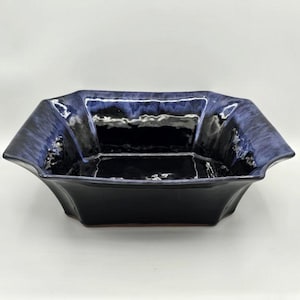 May include: A square ceramic bowl with a dark blue glaze. The bowl has a unique, angular shape with flared sides and a glossy finish. The interior is a deep, reflective black.