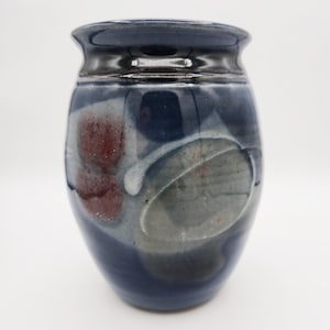 May include: A handcrafted ceramic vase with a dark blue exterior and a glossy finish. The vase features abstract designs in shades of red, gray, and white. The vase has a rounded body and a slightly flared rim, perfect for displaying flowers.