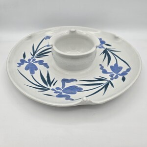 May include: A white ceramic serving platter with a central dip bowl. The platter is decorated with blue floral and leaf designs. The dip bowl is surrounded by a circular serving area with a slightly raised edge.