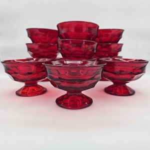May include: A collection of ruby red glass dessert bowls. The bowls have a pedestal base and a faceted design. The bowls are arranged in a group, showcasing their color and shape. The glassware is suitable for serving desserts.