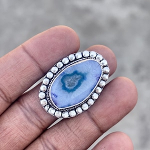 Puede incluir: Anillo ovalado de plata con una piedra de ágata azul claro y blanca. La piedra tiene un patrón único con un centro azul más oscuro. El bisel del anillo está adornado con pequeñas cuentas redondas de plata.