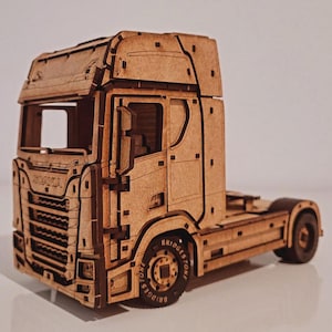 May include: A wooden model of a Scania semi-truck. The truck is constructed from light brown wood and features intricate details, including the Scania logo, Bridgestone tires, and a detailed cab design. The model is a detailed replica of a semi-truck.