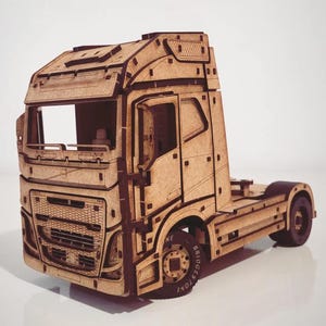 Puede incluir: Maqueta de madera de un camión con detalles intrincados. El camión presenta una cabina detallada, un enganche de remolque y ruedas con la palabra "Bridgestone" en los neumáticos. El modelo está construido con madera de color marrón claro.