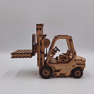 Könnte beinhalten: Ein Holzmodell eines Gabelstaplers mit detailliertem Design. Der Gabelstapler hat eine Hebebühne, einen Fahrersitz und Räder. Das Modell besteht aus hellbraunem Holz und steht vor einem schlichten Hintergrund.