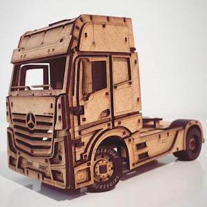 May include: A detailed wooden model of a Mercedes-Benz Actros semi-truck. The model is constructed from light brown wood with intricate cut-out details, including the Mercedes-Benz logo on the front. The tires have the Bridgestone logo. The model is approximately 30 cm long.