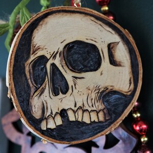 K&ouml;nnte beinhalten: Ein Holzschmuckst&uuml;ck in Form eines Sch&auml;dels mit einem schwarz-wei&szlig;en Design. Der Sch&auml;del ist in das Holz geschnitzt und hat ein detailliertes Design.