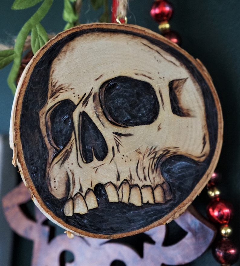 K&ouml;nnte beinhalten: Ein Holzschmuckst&uuml;ck in Form eines Sch&auml;dels mit einem schwarz-wei&szlig;en Design. Der Sch&auml;del ist in das Holz geschnitzt und hat ein detailliertes Design.