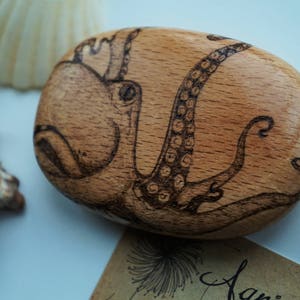 May include: A wooden coaster with a hand-drawn image of an octopus in black ink. The octopus is curled up with its tentacles visible.